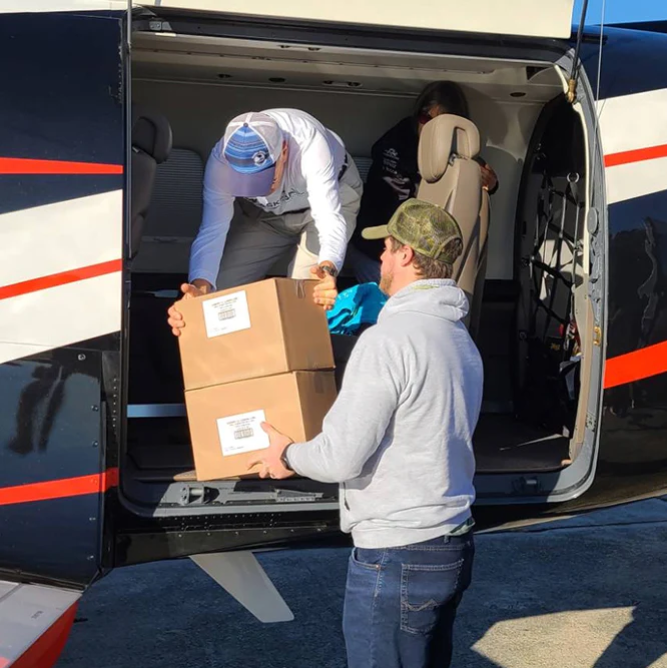 Two men loading boxes of supplies into a small airplane for delivery