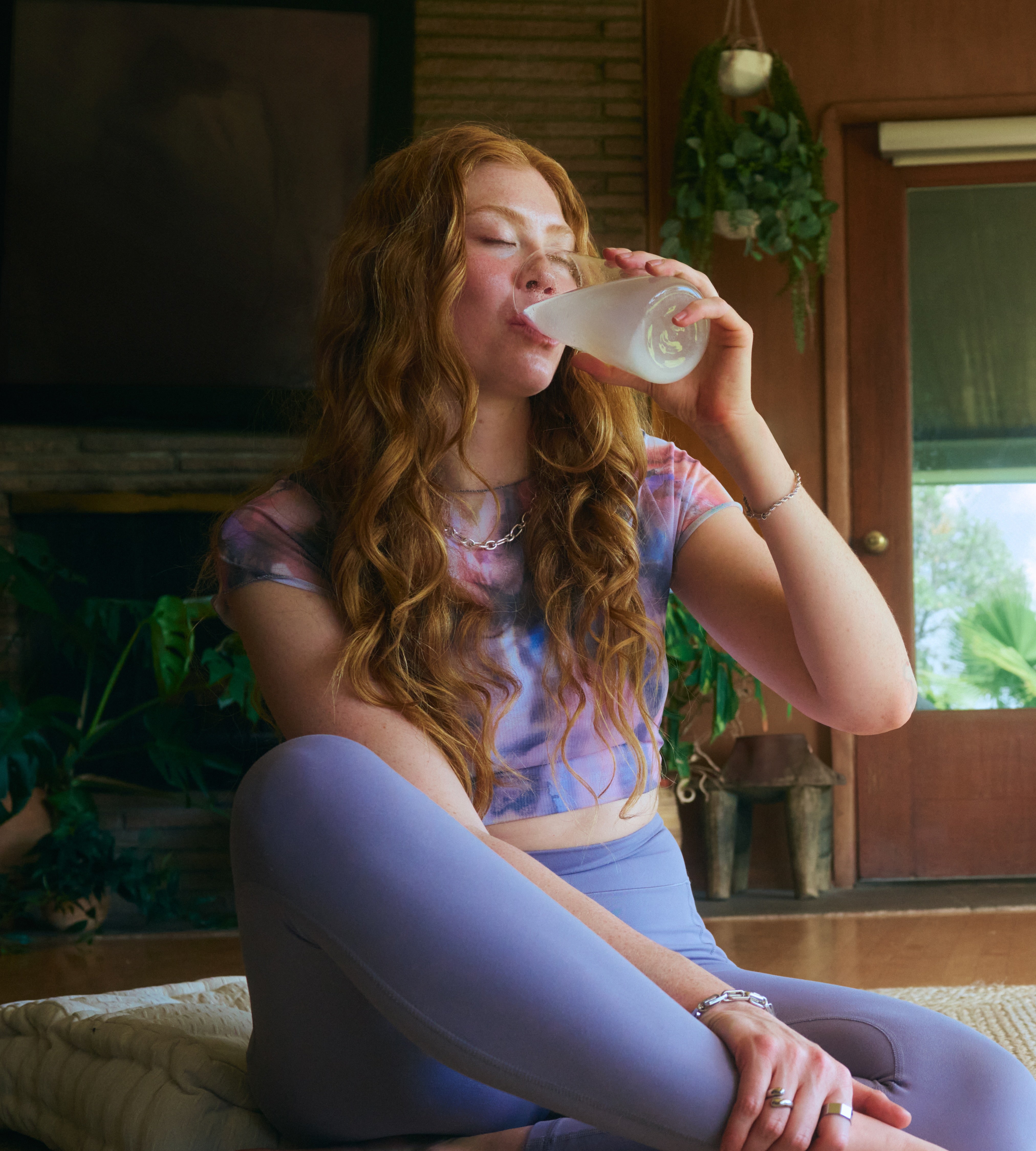 Woman sitting on a mat in a cozy living room, drinking Liquid I.V. for hydration and relaxation