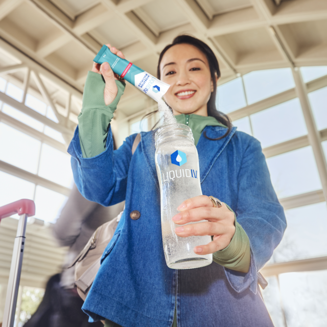 Smiling woman holding a Liquid I.V. bottle with a hydration stick, ready to mix